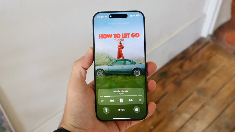 A hand holding an iPhone with Apple Music animated cover in the Lock Screen
