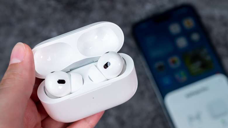 A hand holding an opened AirPod case with AirPods inside