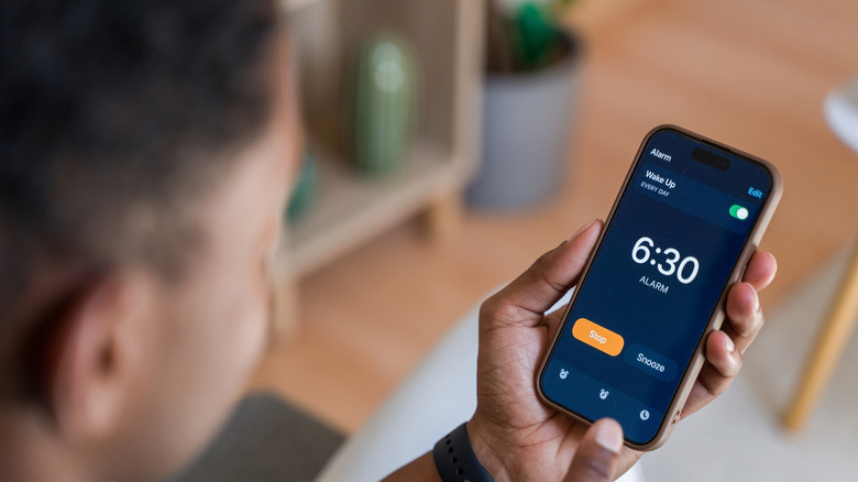 man looking at smartphone alarm clock settings