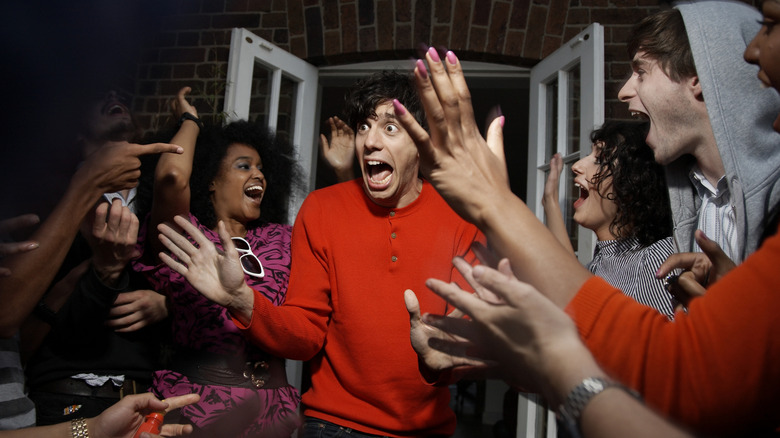 A man looking surprised as he walks in a door and people surround him yelling surprise.