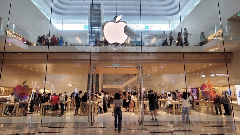 A busy Apple Store in a luxury shopping mall featuring a sleek glass facade