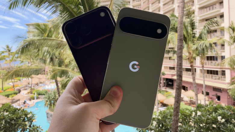 iPhone 18 Pro Max and Pixel 11 Pro XL being held in one hand against greenery in background