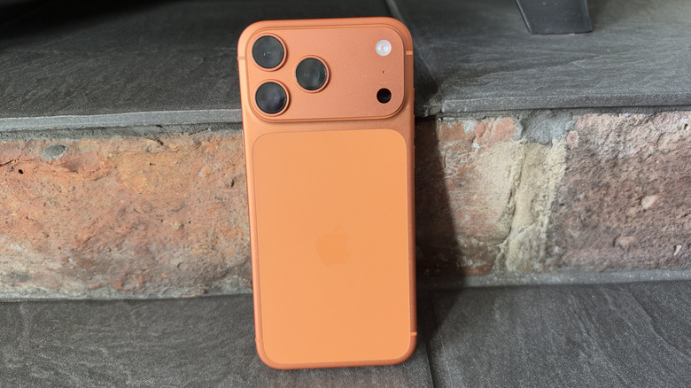 iPhone 17 Pro Max in Cosmic Orange leaning against bricks