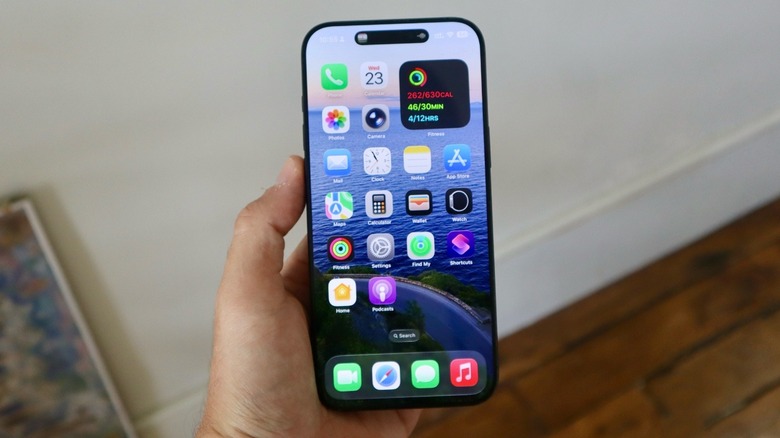A hand holding an iPhone with the Home Screen on