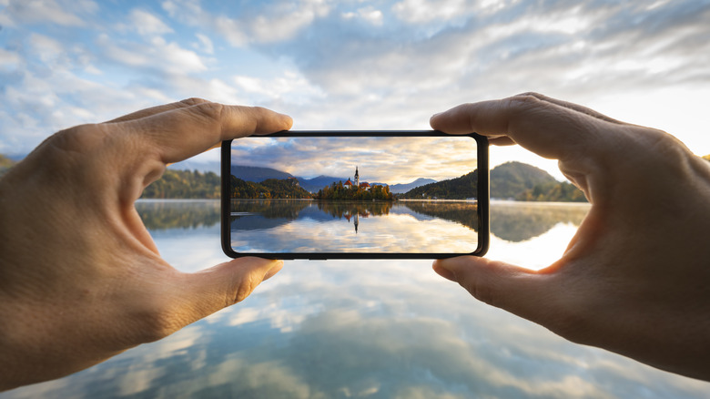 A photo of someone holding an iPhone taking a picture of a scenic lake landscape.