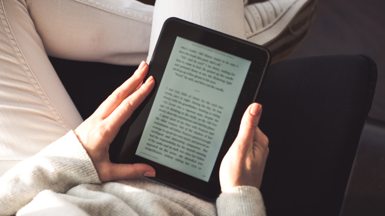 Person holding an e-reader while reading an ebook on a couch.