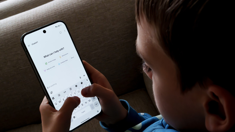 A kid readies to type into a ChatGPT application on their phone, where the words "What can I help you with?" are prominently displayed.
