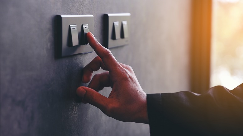 A hand reaches for a switch to turn off the lights in a room