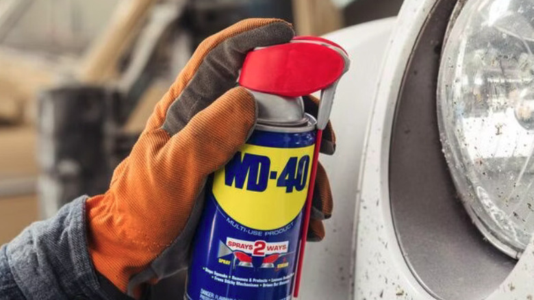 A mechanic using a can of WD-40 to spray on a headlight cover.