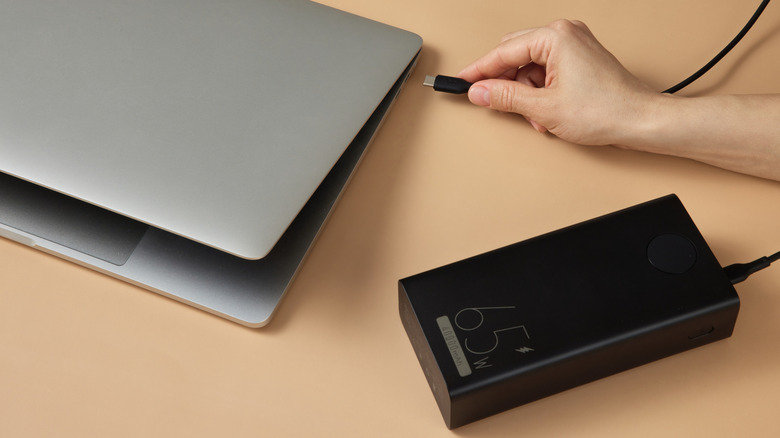 A hand plugging a cable from a power bank into a laptop
