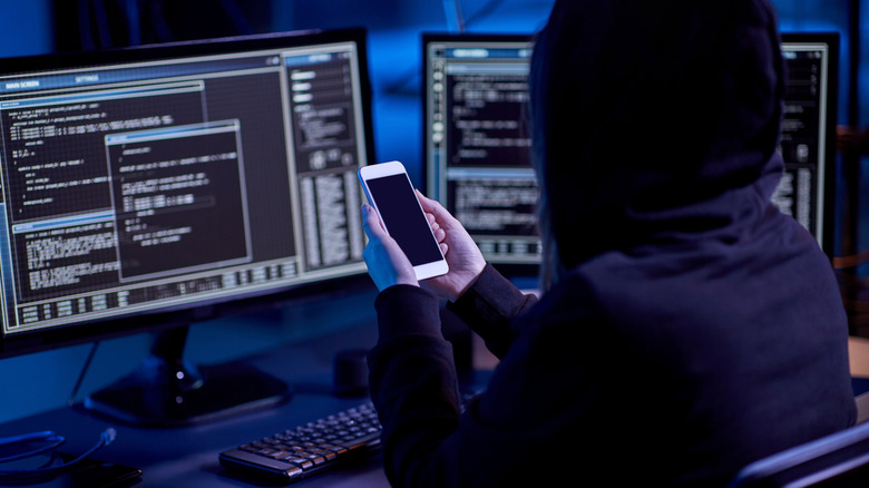 hacker with smartphone using computer virus program for cyber attack in dark roo