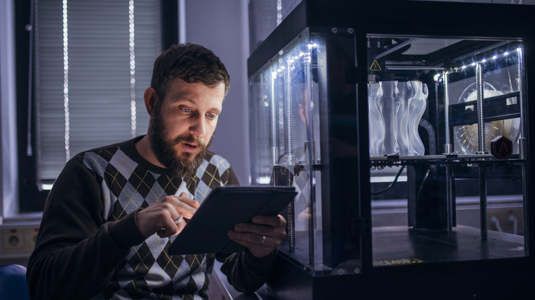 Man on a tablet next to an enclosed 3D printer with a project in progress.