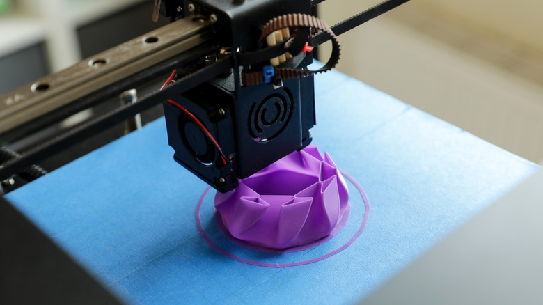 Close up view of a 3D printer creating a purple and elliptical object.