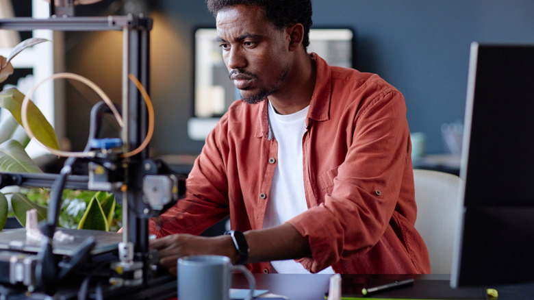 Man working on a 3D printer in an office setting.