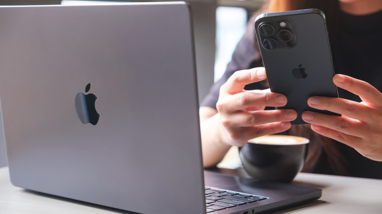 A woman using an iPhone, with a MacBook open next to her.