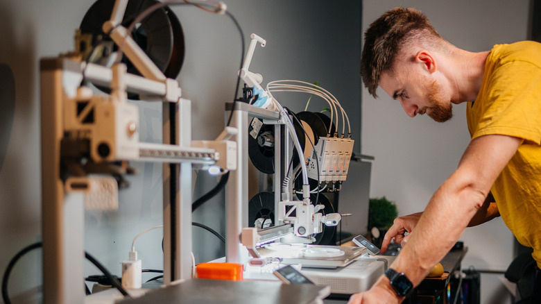 person operating a 3d printer with another kept on the side