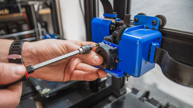 person using a screwdriver to tighten the screws on a 3d printer