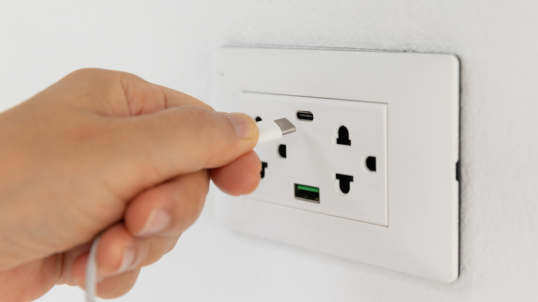 A person inserting a USB-C cable into a wall outlet with USB-C and USB-A ports.