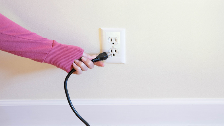 User plugging a three-pronged power connector into a compatible wall socket.