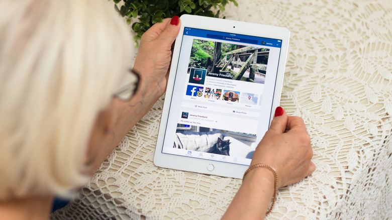 An old person sits near the desk, holding iPad Air