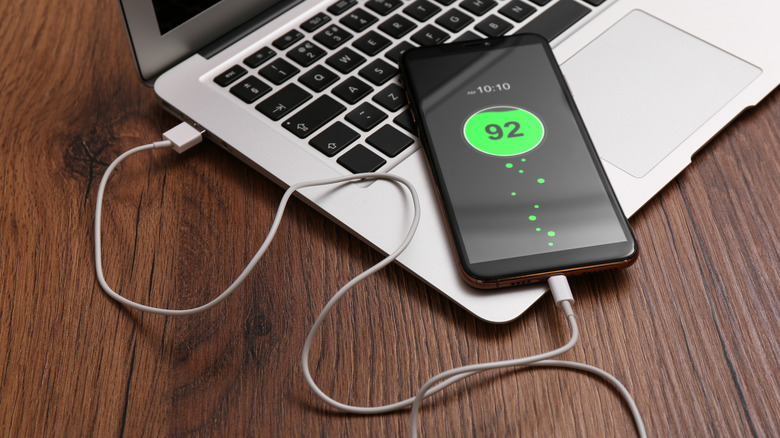 A phone connected to a laptop for charging on a wooden table