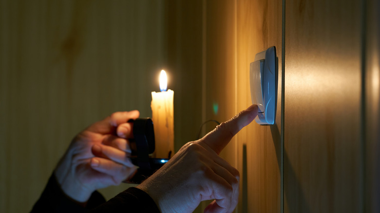 A person holding a candle and pressing a button in the case of a blackout