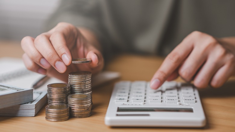 A person stacking coins next to a calculator.