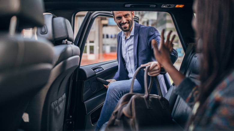 People getting into the back of a car with luggage in hand.
