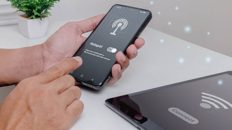 Person holding a smartphone sharing internet with a tablet kept on a white table using hotspot