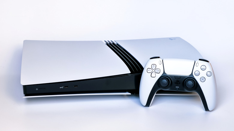 A PS5 Pro laid horizontally on a white surface with a PS5 DualSense controller in front of it.