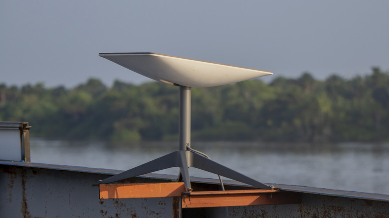 Starlink satellite internet dish mounted on a metal platform near a river, with trees in the background.