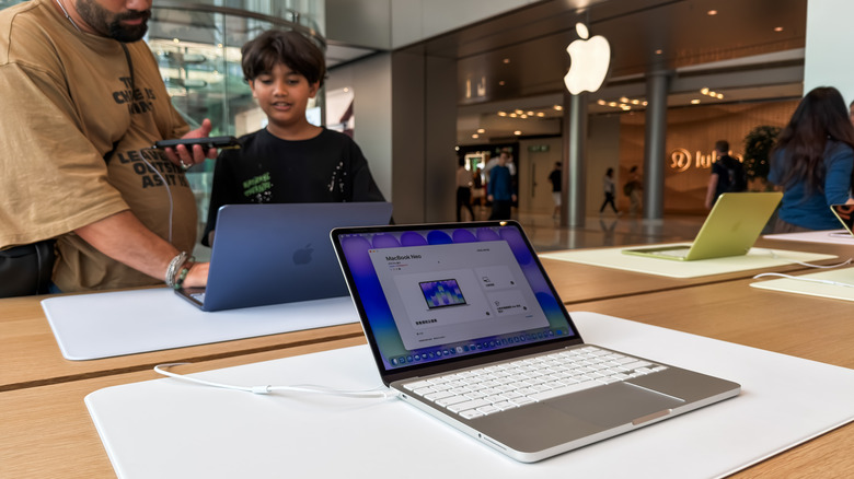 People testing a MacBook Neo laptop inside of an Apple store.