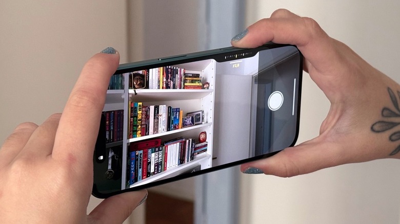 A woman taking a photo of a bookshelf with the iPhone 16 Camera Control functionality