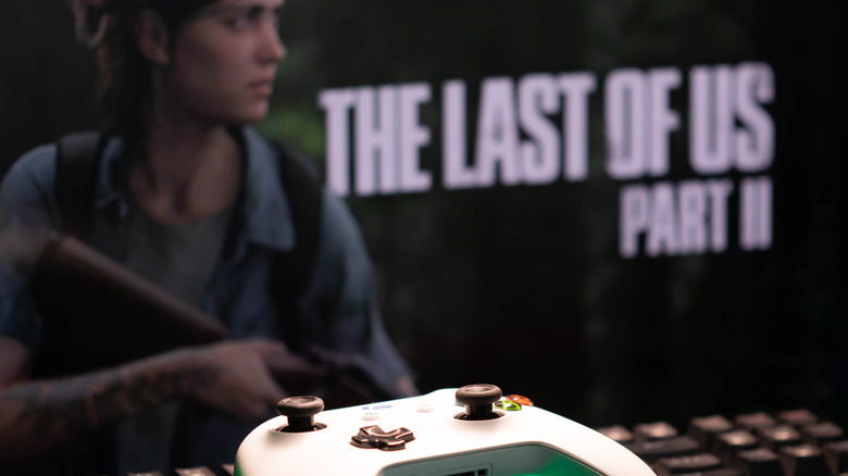 An Xbox controller in front of a poster for The Last of Us Part II.