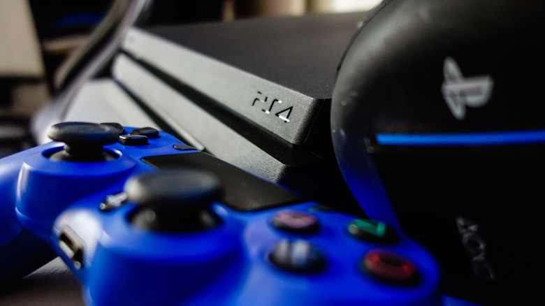 A PlayStation 4 Pro behind a blue controller and a black headset