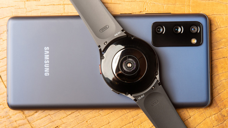 Samsung Galaxy Watch 4 on top of a Samsung Galaxy S20 FE phone on a wooden table