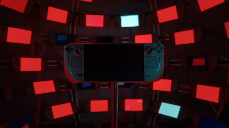 A powered off Steam Deck held up by a pole in front of other Steam Decks displaying solid red and white screens