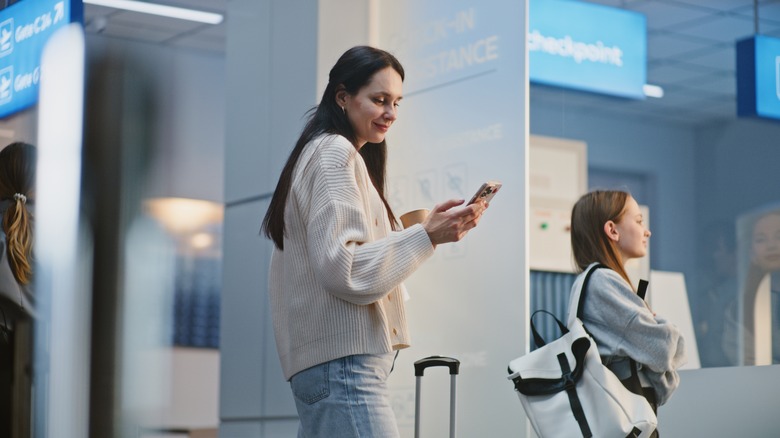 Mother using smartphone in airport with daughter nearby.