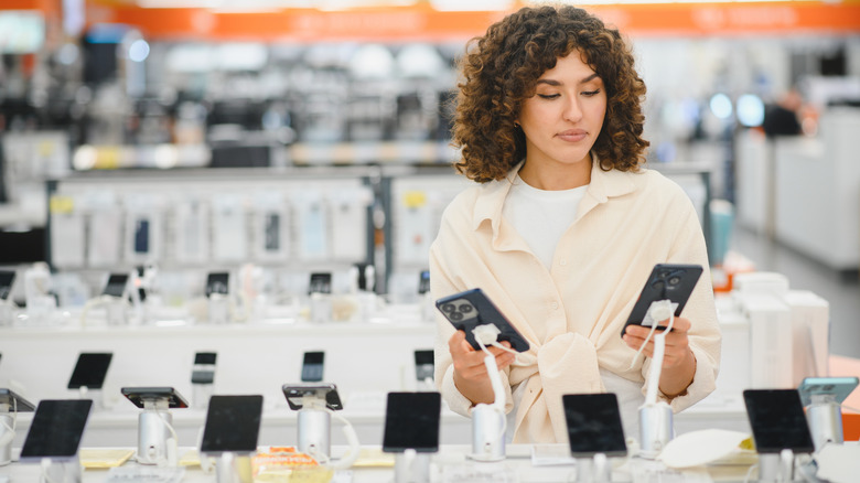 A woman comparing smartphones at an electronics store.