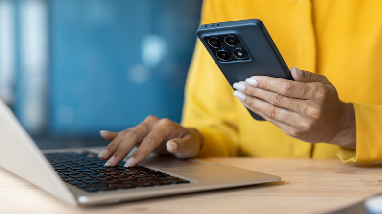 A person holding a smartphone and browsing on a laptop