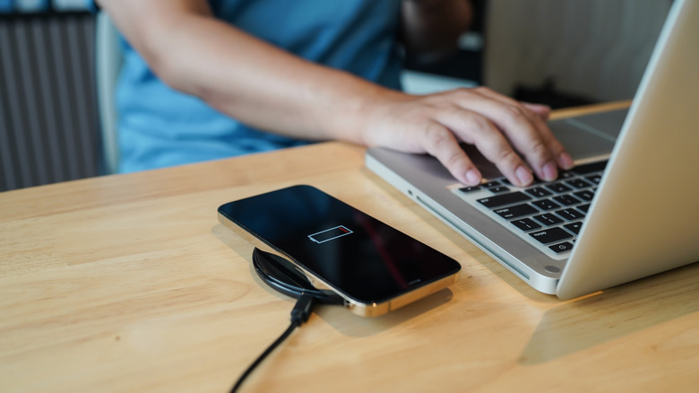 A drained iPhone being charged with a wireless charger while on a desk