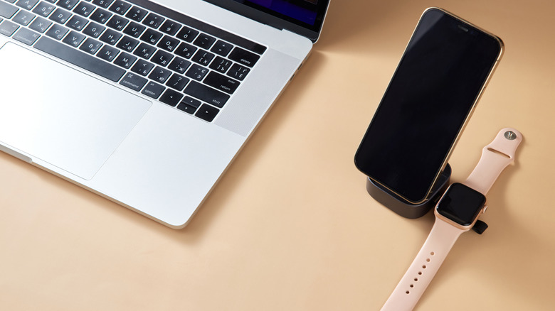 An iPhone and Apple Watch on wireless chargers while next to a MacBook