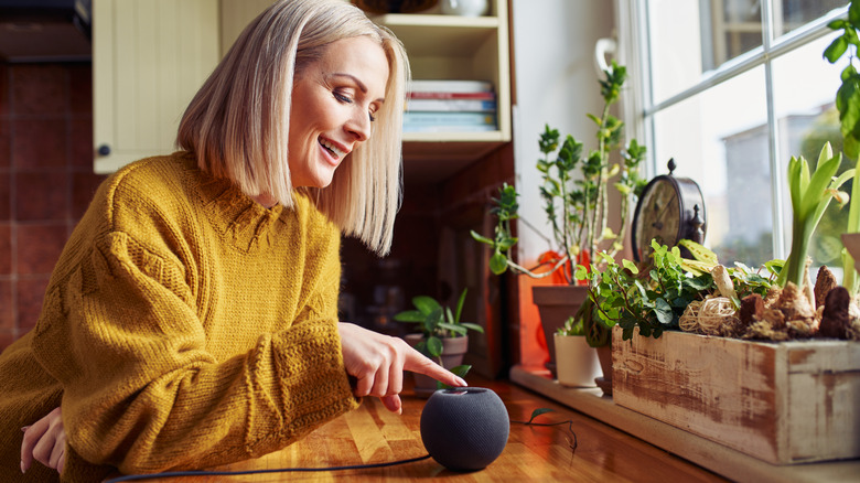 A woman touching a button on the top of a smart speaker in her kitchen.