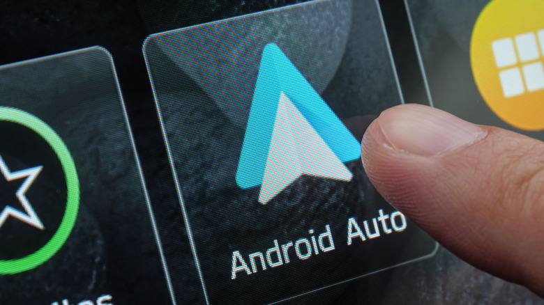 Close-up view of a finger pressing the Android Auto icon on a car's dashboard