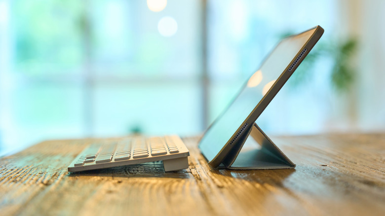Close up of a tablet with a wireless keyboard in front of it, resting atop a wooden table.