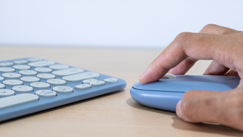 Hand using a wireless mouse with the edges of a matching wireless keyboard nearby.