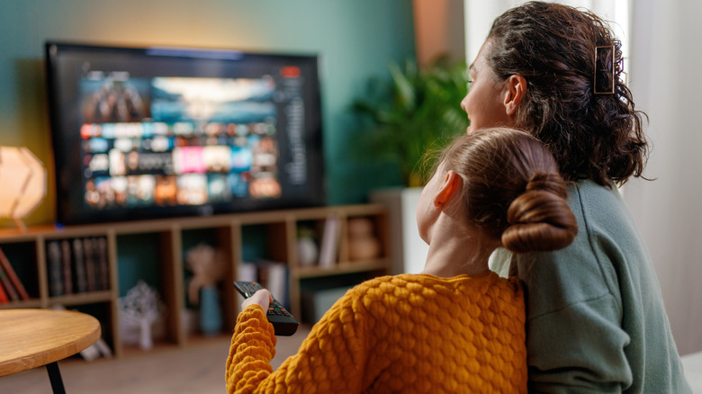 A mom and daughter cuddling together on the couch watching TV