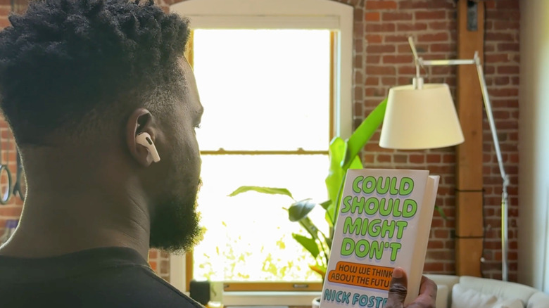 A man wearing AirPods holding up a book and looking at it