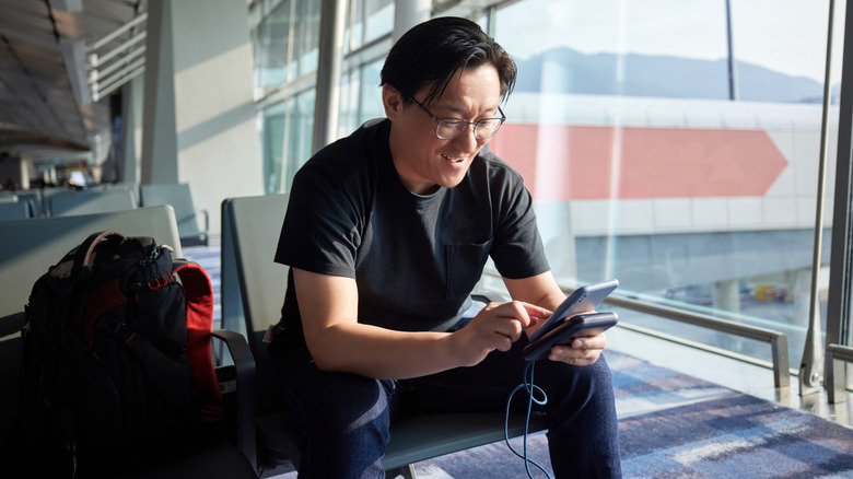 Person seated in an airport using a phone that's connected to a portable power bank
