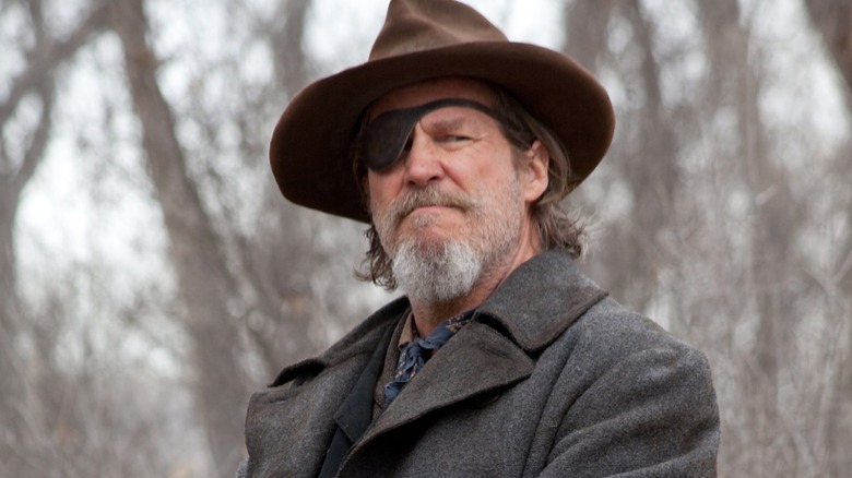 Jeff Bridges as Rooster Cogburn in front of trees in True Grit